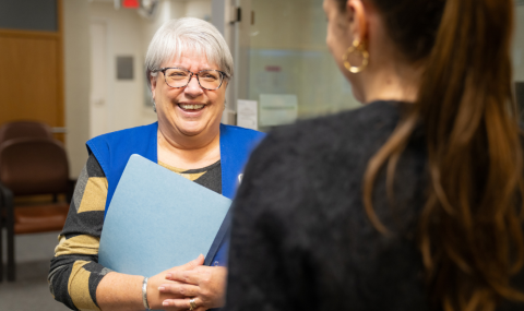 Kathy McGuire talks with an individual while standing at the volunteer desk in the Verspeeten Family Cancer Centre