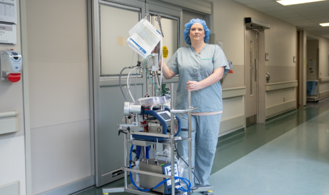 Crystal Engelage, Research Associate, in front of the operating room with the pump used to recirculate blood and oxygen to organs.