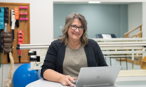 Patrice Green smiling sitting infront of laptop wearing an olive green shirt and black sweater