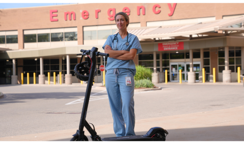 Dr. Belisle in scrubs standing outside Emergency department with an escooter in front of her