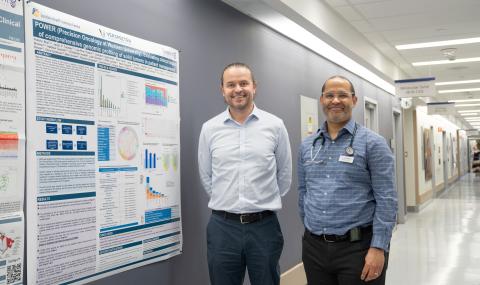 Two researchers stand beside a poster presenting findings from the POWER study in a hospital research corridor.