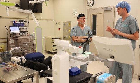 Dr. Timothy Carey and Dr. Patrick Thornley, Paediatric Orthopaedic Surgeons at London Health Sciences Centre (LHSC) standing behind with a Mazor robotic platform in an operating room.