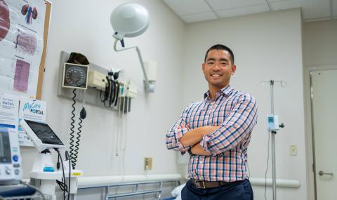 Dr. Michael Chiu stands beside an examination table and medical equipment in a hospital examination room.
