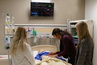 Three women practice giving care to a dummy