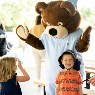 Image of two children playing with a bear mascot 