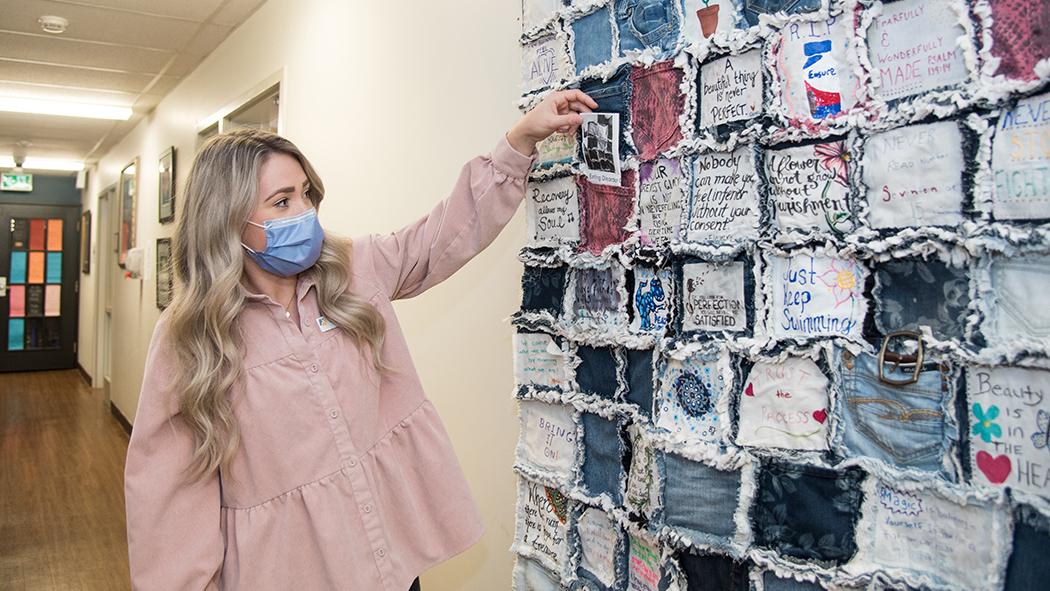 Image of Jenah St-Jacques, AEDS Dietitian, places a denim patch on the quilt that provides inspirational messaging to all patients.