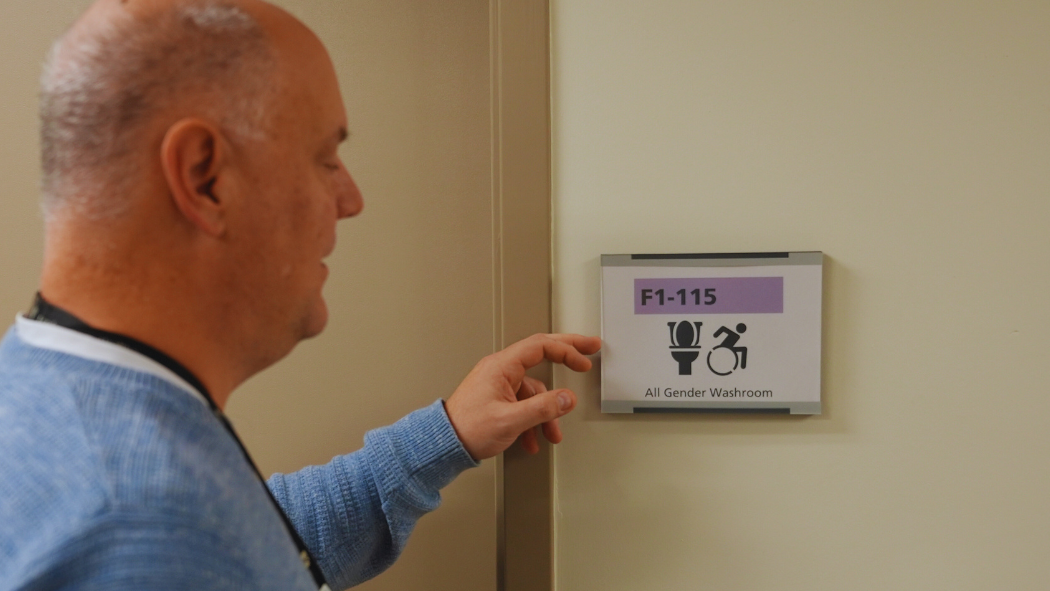 A facilities worker installing an all gender washroom sign