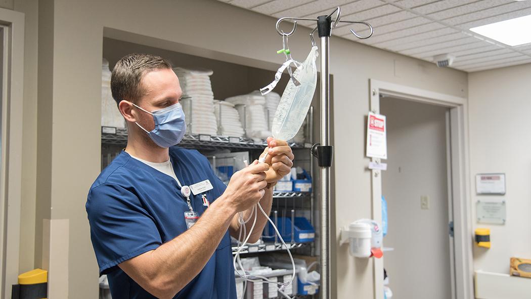 Nursing student Adrian Roes primes an IV line for a patient as he begins his final placement.