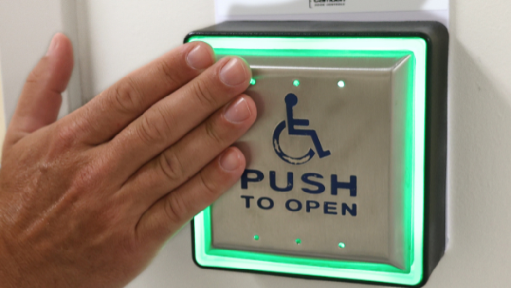 A photo of a hand touching a button to open a wheelchair accessible door.