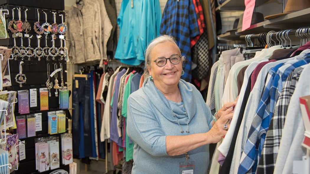 Lyn Harrison, president of the London Health Sciences Centre Auxiliary, stands in the Tower Shoppe at Victoria Hospital. She's surrounded by products from the gift shop and is touching clothing on display.