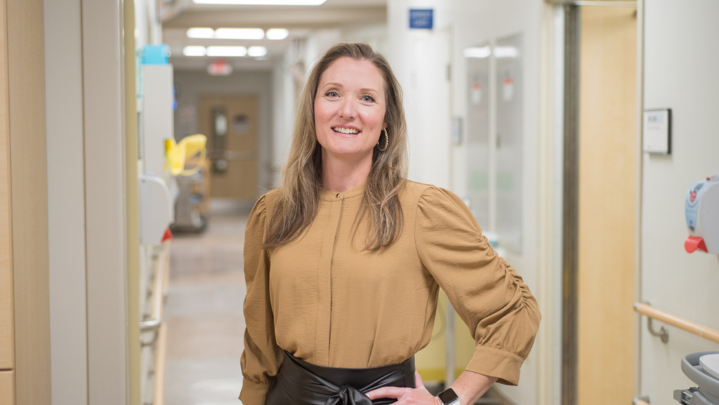Melanie Watson wearing a yellow-gold shirt standing in the hallway of a paedatric unit in the hospital