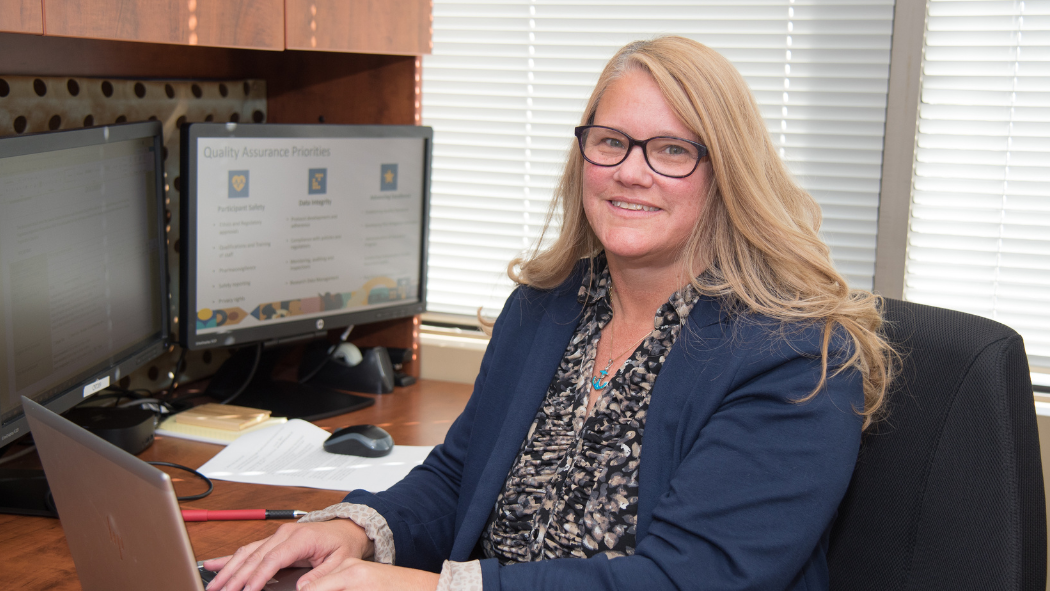 staff member smiles at camera while sitting at desk working