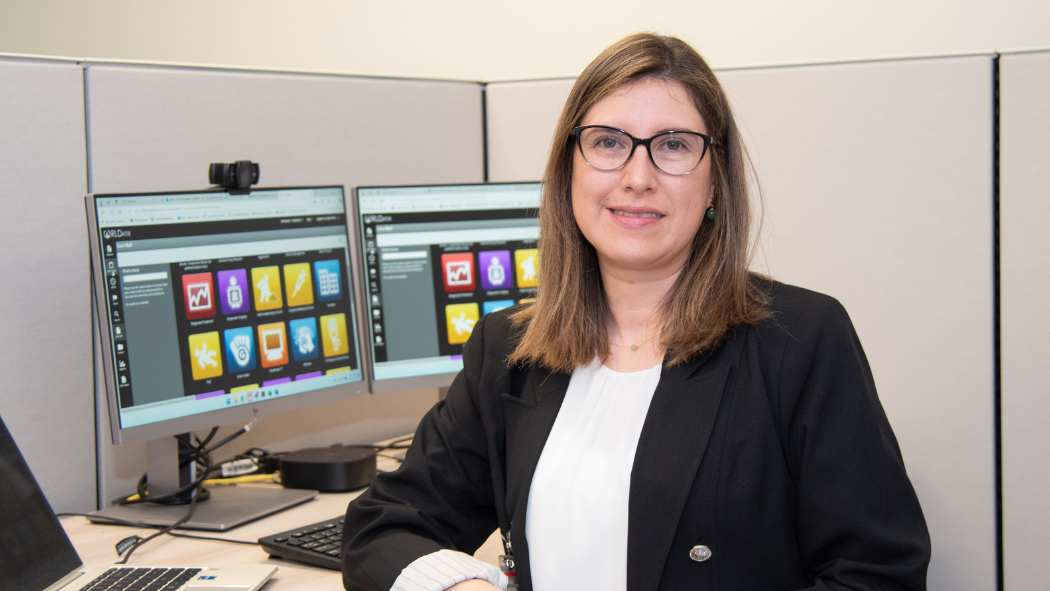 Woman smiling at camera stands in front of computer screen