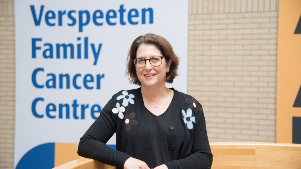 Dr. Joy Mangel stands in front of a Verspeeten Family Cancer Centre banner