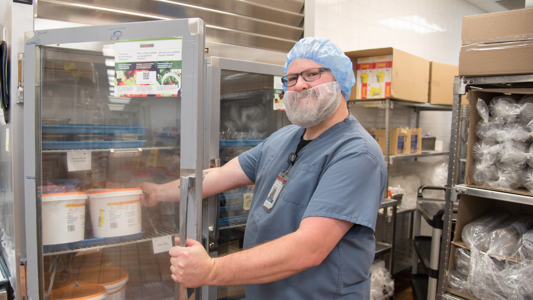Food services worker smiles at camera while opening a fridge