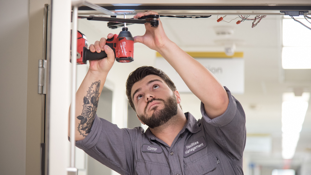 Facilities team member uses a screwdriver on a door frame