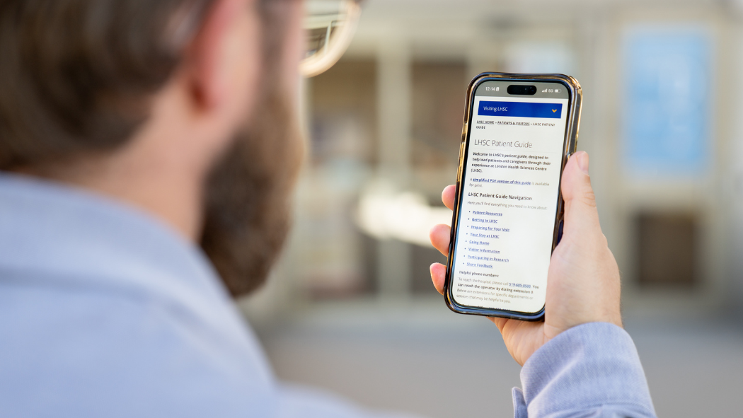 A person holding a smartphone and viewing a webpage titled “LHSC Patient Guide” while standing outdoors.