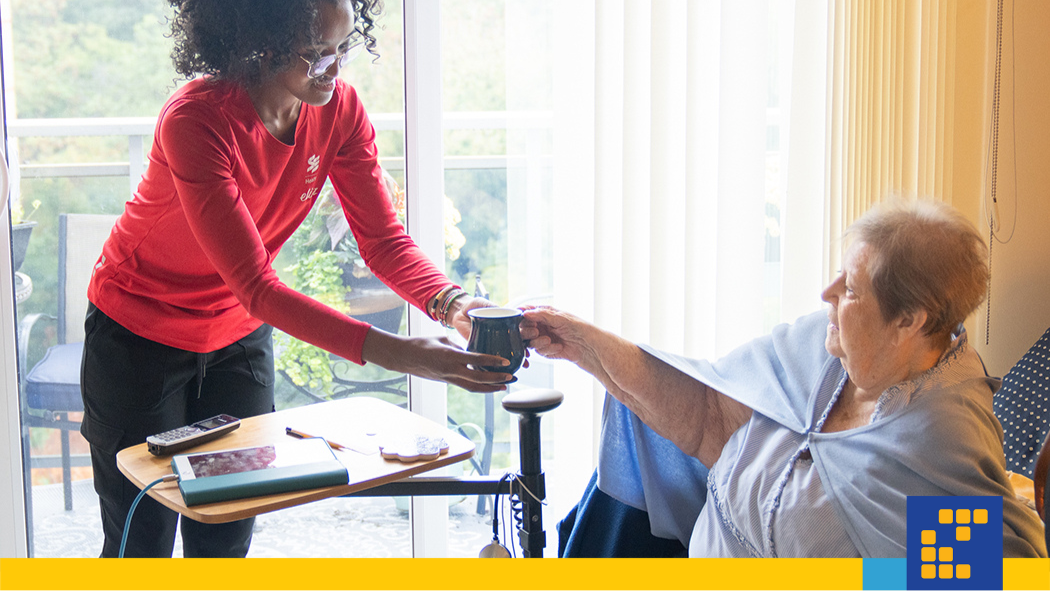 A young Personal Support Worker hands a patient a cup of tea.