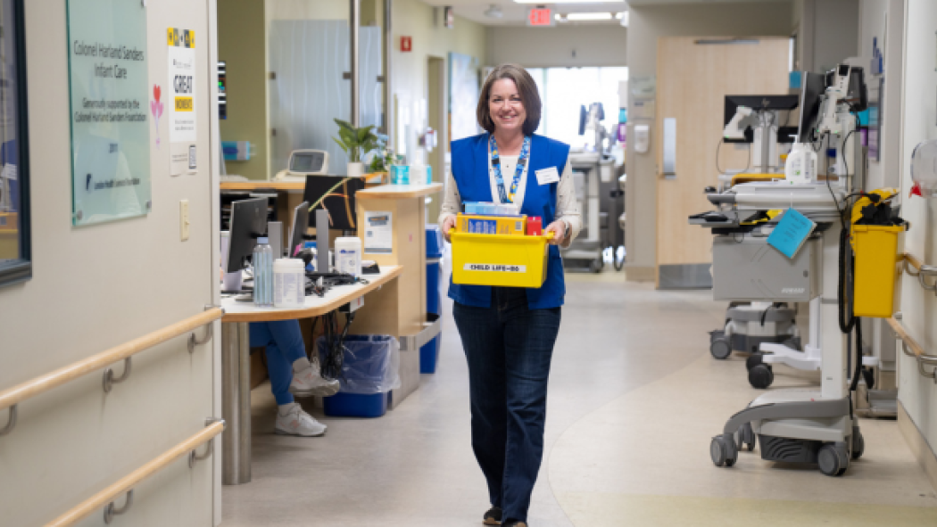 Carroll walks down the hallway on the Paediatric Inpatient Unit carrying a bin of toys.