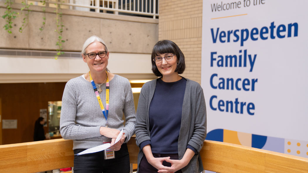 Two female oral chemotherapy pharmacists stand smiling at camera