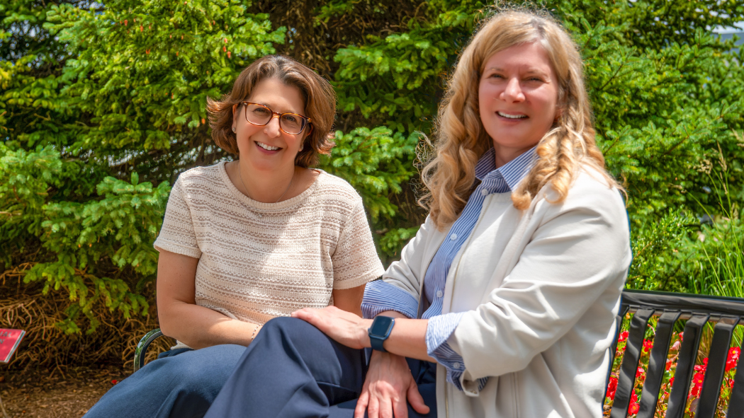 Two women sitting on a garden bench smiling