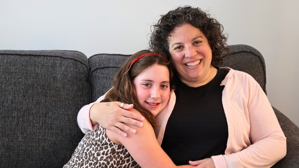 Stella in a leopard print shirt hugging her mom, Sari, wearing a black shirt and pink sweater
