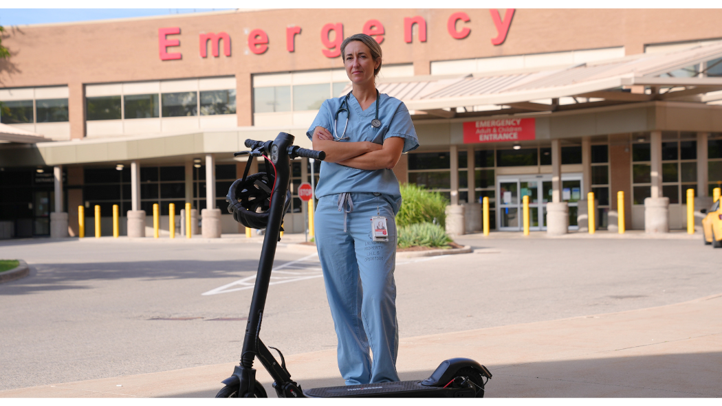 Dr. Belisle in scrubs standing outside Emergency department with an escooter in front of her