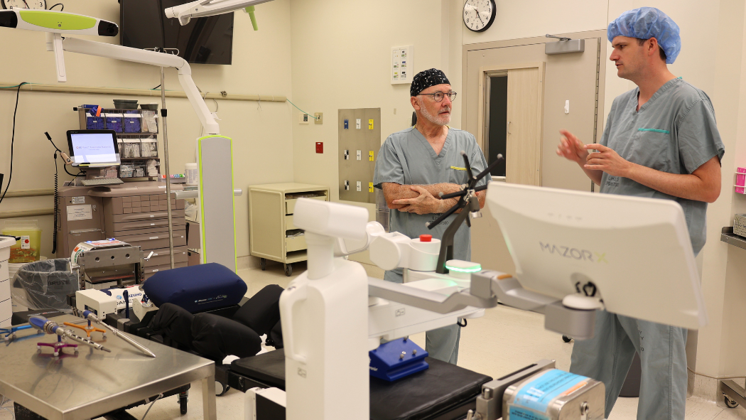 Dr. Timothy Carey and Dr. Patrick Thornley, Paediatric Orthopaedic Surgeons at London Health Sciences Centre (LHSC) standing behind with a Mazor robotic platform in an operating room.